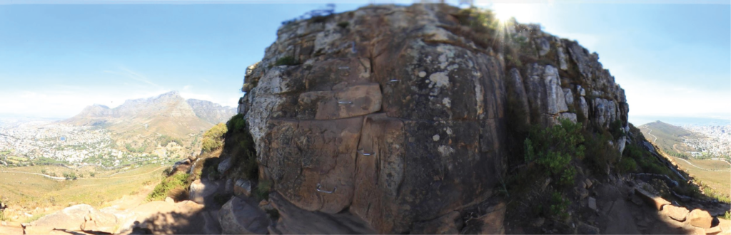 Ca. 2 Meter hohe rotbraune Felswand mit eingeschlagenen Eisenklammern und Ketten, um daran hochzuklettern