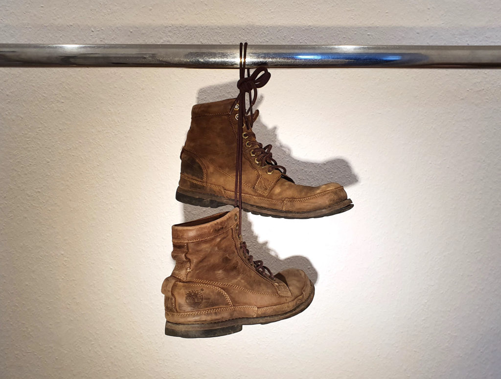 Ein Paar stark abgenutzter Lederstiefel von Timberland, Modell Earthkeepers 6-Inch-Stiefel, an den Schnüren zusammengebunden und über eine verchromte Stange gehängt.