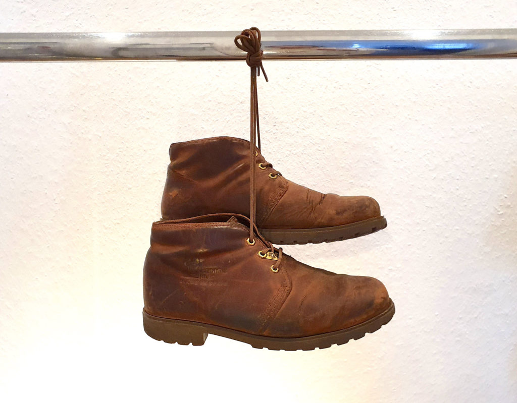 Ein Paar gebrauchte Lederstiefeletten von Panama Jack, Modell BOTA PANAMA, an den Schnüren zusammengebunden und über eine verchromte Stange gehängt.