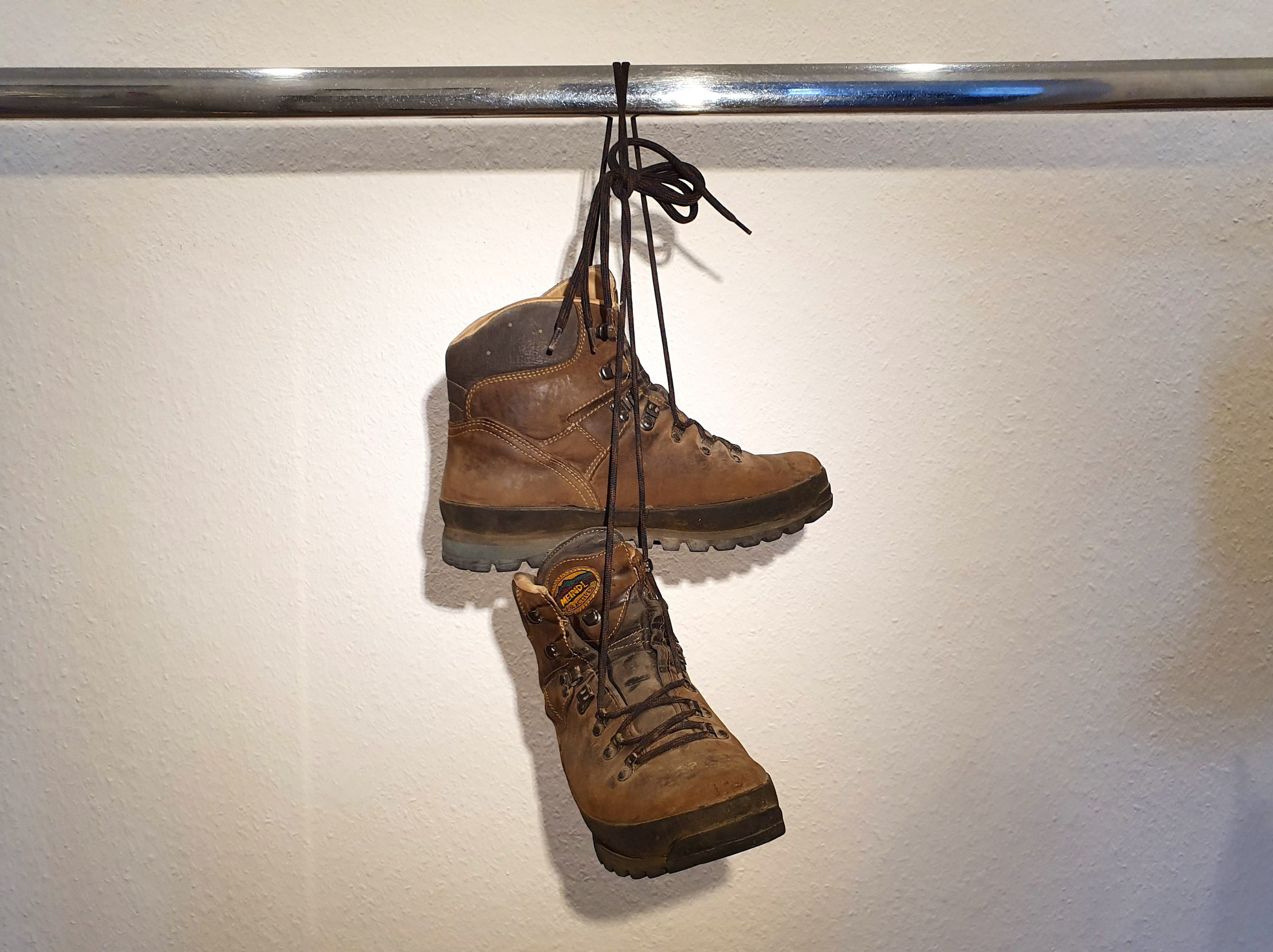 Ein Paar gebrauchte Wanderstiefel von Meindl, Modell BORNEO 2 MFS, an den Schnüren zusammengebunden und über eine verchromte Stange gehängt.