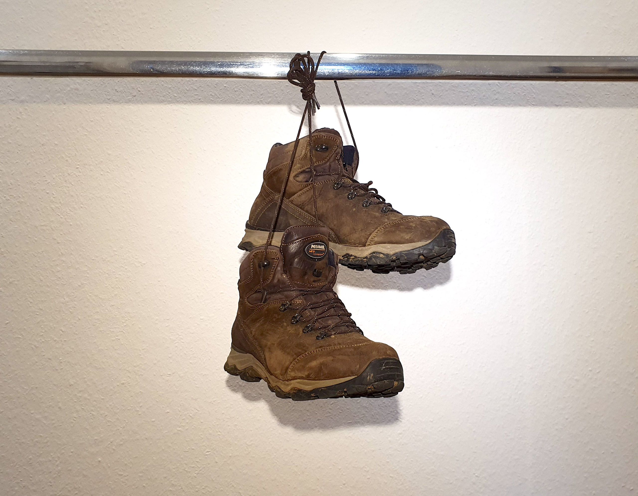 Ein Paar gebrauchte Wanderstiefel von Meindl, Modell Eppan GTX Mahagoni, an den Schnüren zusammengebunden und über eine verchromte Stange gehängt.